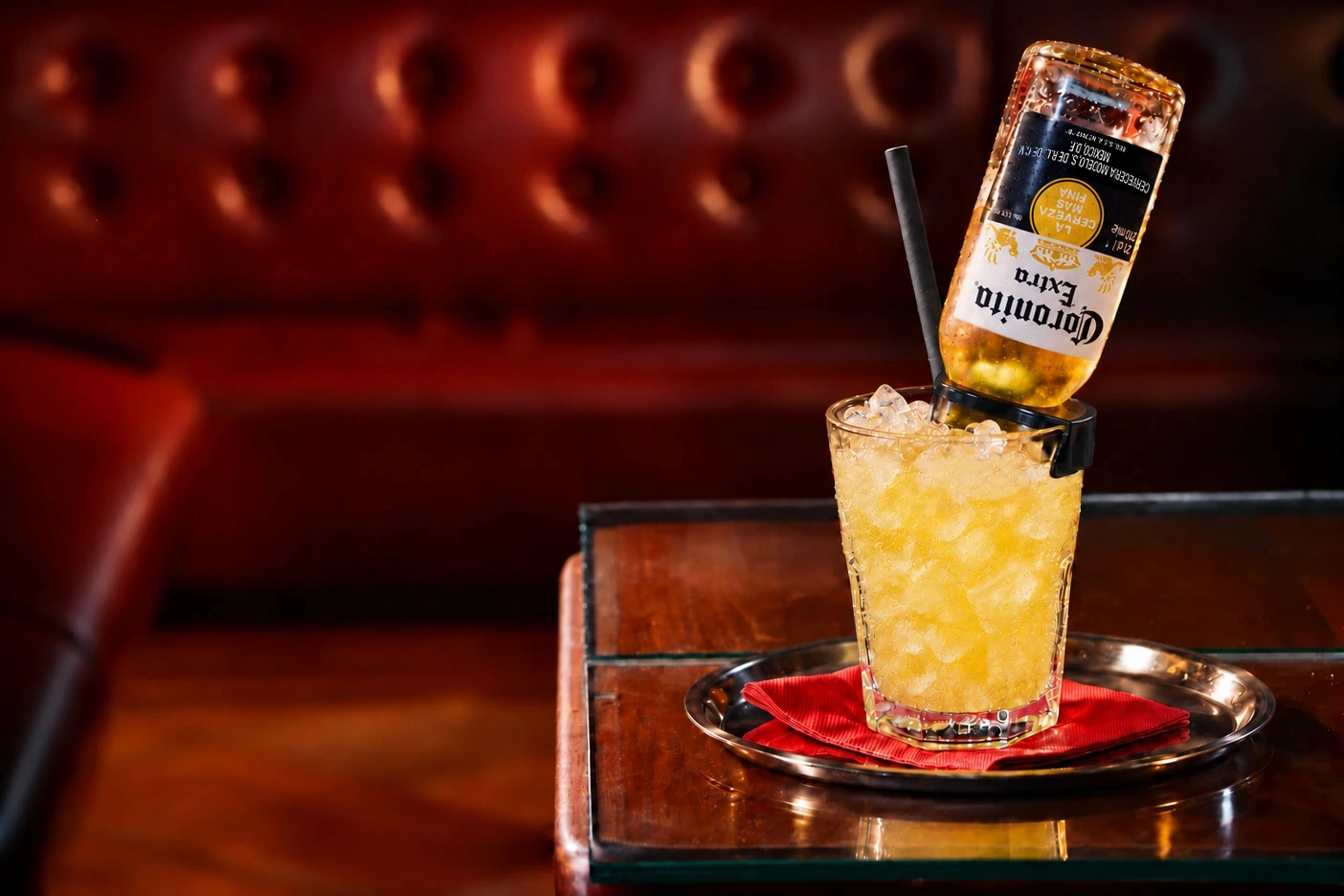 Coronita mit Crushed Ice, kopfüber eingesetzter Coronita-Flasche und schwarzem Papierstrohhalm